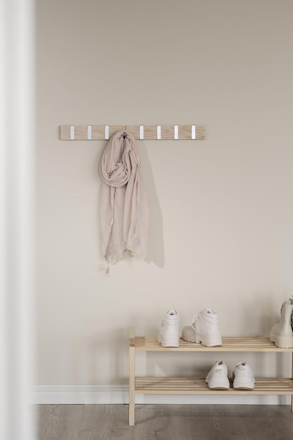 Ljus trähängare med vita krokar monterad på vägg, beige scarf hängande, träskoställ med vita sneakers nedanför