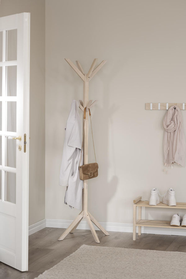 Ljus träklädhängare i hall med vit dörr, med jacka och väska upphängd, skoställ och väggkrokar vid sidan