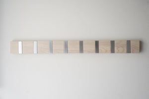 Krokсписок av ljust trä med sju metallkrokar i gradient från vit till mörkgrå monterad på vit vägg
