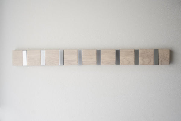 Krokсписок av ljust trä med sju metallkrokar i gradient från vit till mörkgrå monterad på vit vägg