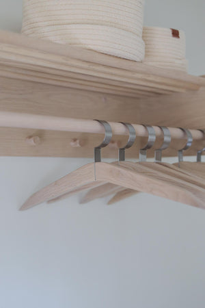 Klädgarderob i ljust trä med metallkrokar och hyllplan, minimalistisk skandinavisk design