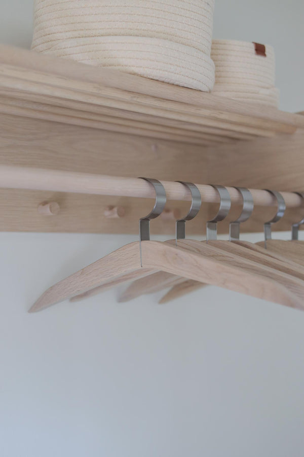 Klädgarderob i ljust trä med metallkrokar och hyllplan, minimalistisk skandinavisk design