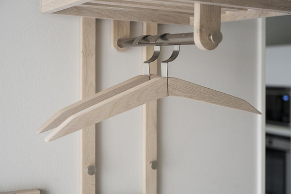 Ljusa trägalgar hängande på utdragbar klädhängare under garderobshylla i naturligt trä