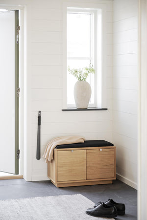 Hallmöbel i ek med svart sits och skåp, placerad under fönster med vit snickeripanel