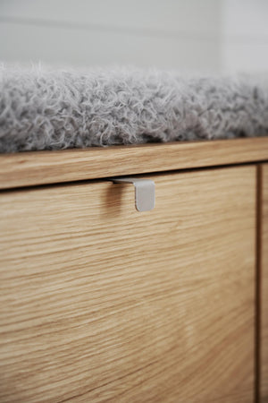 Närbild på träbyrå med synlig trästruktur, metallhandtag och grå filt på toppen
