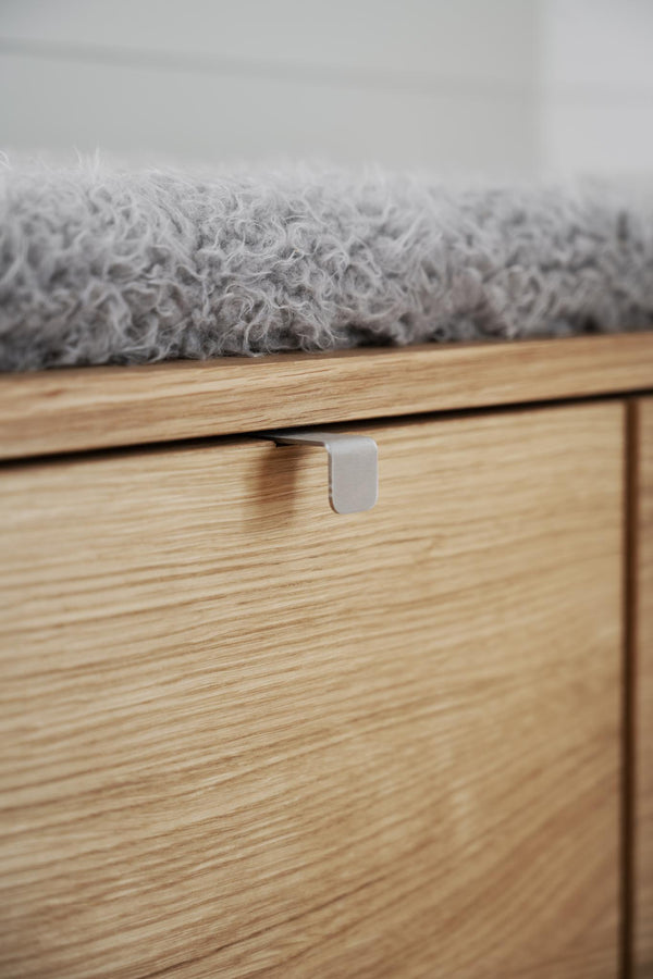 Närbild på träbyrå med synlig trästruktur, metallhandtag och grå filt på toppen