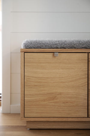 Sittbänk i ekfanér med förvaring och grå fårskinnsdyna mot vit vägg