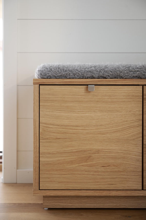 Sittbänk i ekfanér med förvaring och grå fårskinnsdyna mot vit vägg
