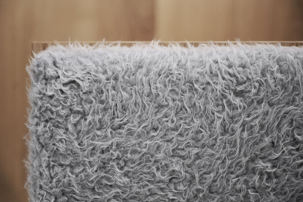 Närbild av grå fluffig textil med lockiga fibrer, möjligen en fuskpäls eller dekorativ matta med mjuk textur