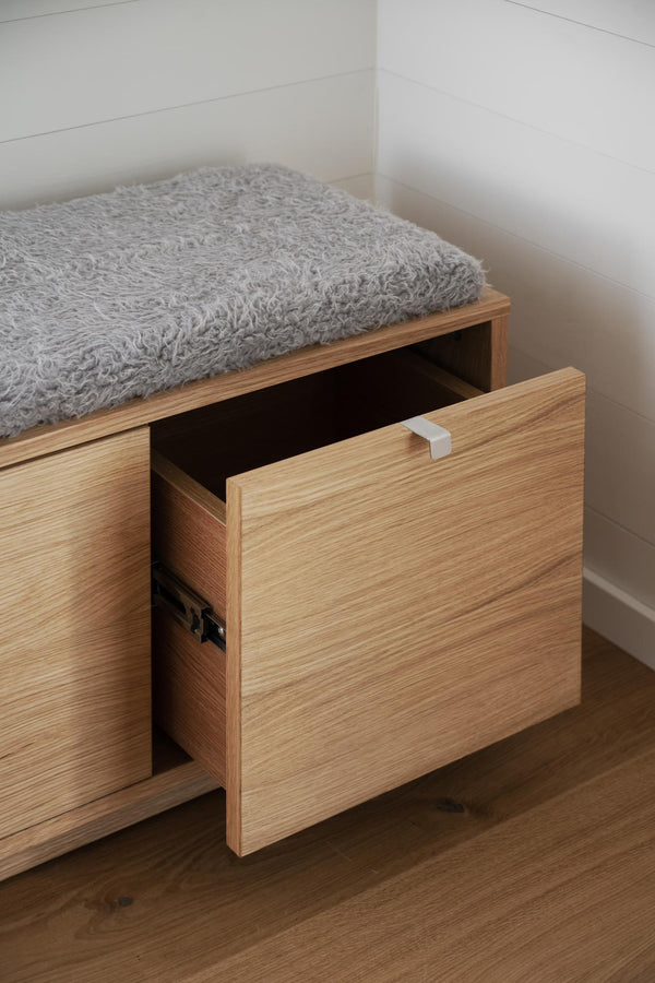 Träbänk med grå kuddyna och utdragen låda med vit knopp i modern skandinavisk design