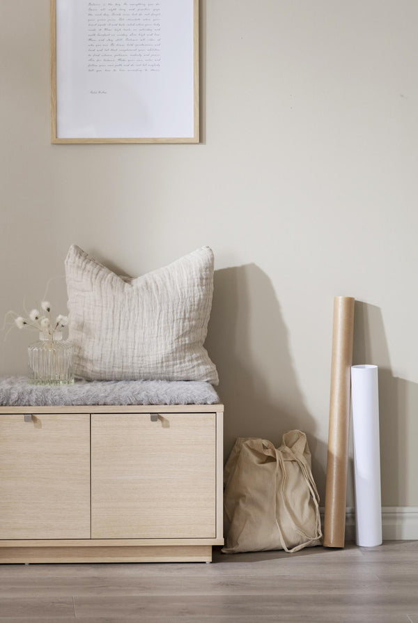 Ljust förvaringsskåp i trä med kudde och dekoration i naturliga toner mot beige vägg