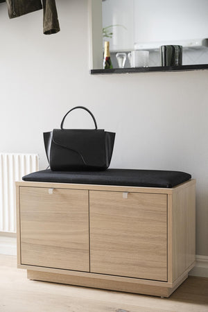 Hallbänk i ekfanér med svart dyna och förvaringsskåp, med svart handväska på sittdynan