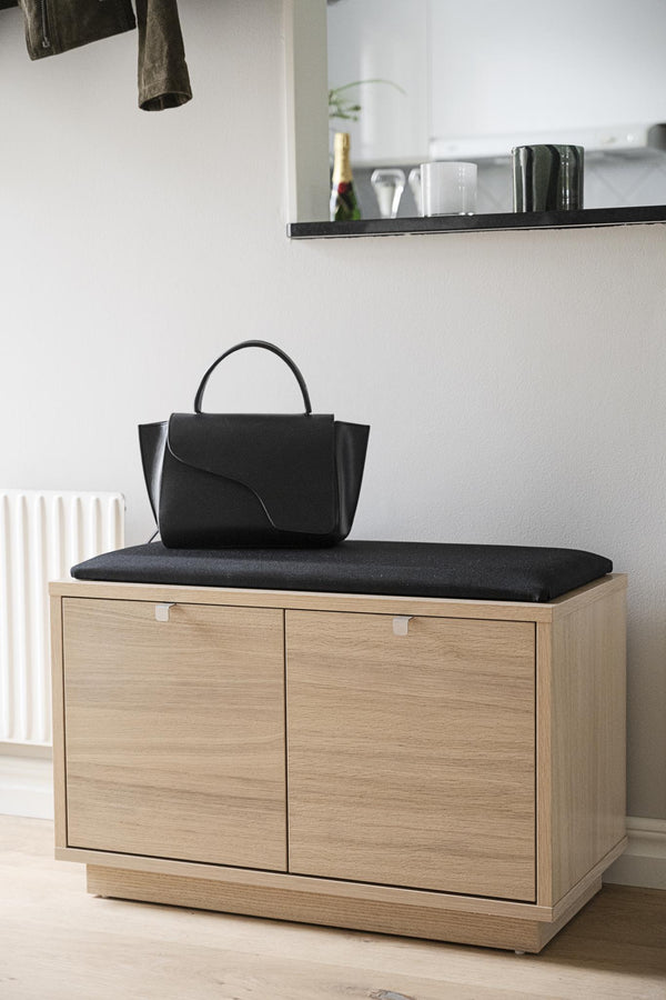 Hallbänk i ekfanér med svart dyna och förvaringsskåp, med svart handväska på sittdynan