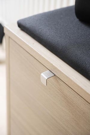 Bänk i ljust trä med grå sits och modern metallhandtag på lådfronten