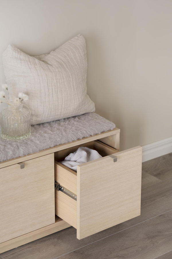 Hallbänk i ljust trä med öppen låda, grå fuskpäls och vit kudde, skandinavisk design