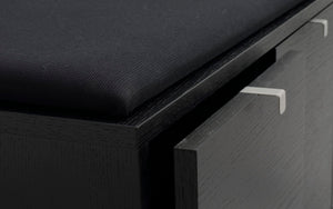 Närbild på svart träskänk med två utdragslådor med moderna stålhandtag och stoppad sits ovanpå