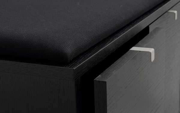 Närbild på svart träskänk med två utdragslådor med moderna stålhandtag och stoppad sits ovanpå