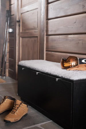 Svart hallbänk med vit dyna, skidutrustning och bruna vinterkängor i modern inredning med trävägg