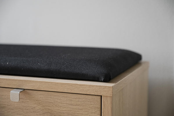 Sittkudde i svart tyg på bänk i ljust trä med låda och rundad handtagsöppning