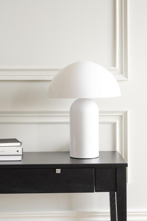 Vit mushroomlampa med cylindrisk bas och kupolformad skärm på svart skrivbord