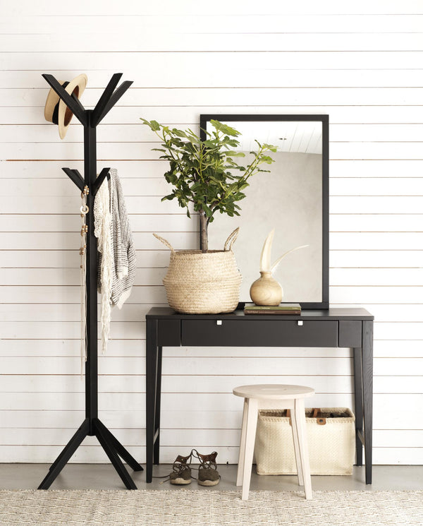 Svart hallmöbel med lådor, spegel, krukväxt i korg och vit pall med förvaringslådor