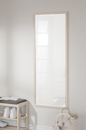 Stor spegel med ljus träram monterad på vit vägg ovanför bänk med handdukar och korg