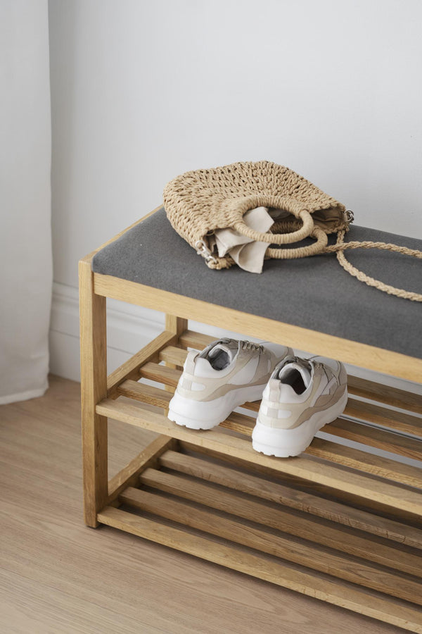 Skoställ i trä med grå toppkudde, vita sneakers på nedre hyllan och virkad väska på överdel