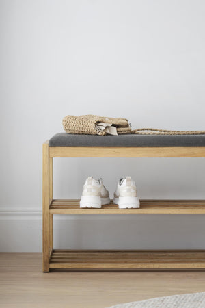 Bänk med skoförvaring i ljust trä med grå dyna, vita sneakers och korg med naturligt material