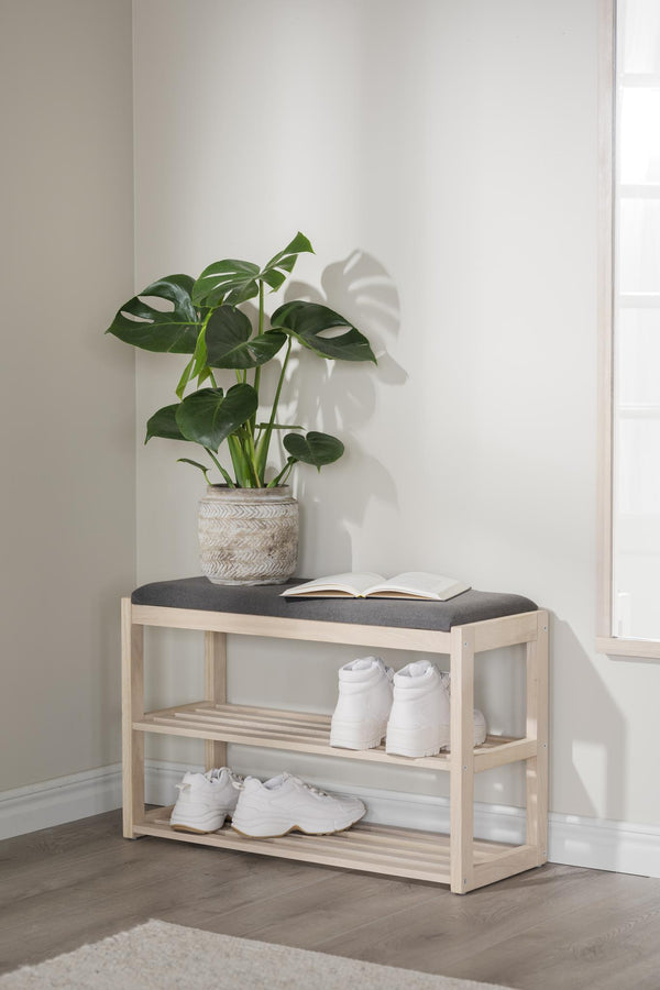 Skoställ i ljust trä med grå sittdyna, två hyllplan med vita sneakers och grön växt i kruka på toppen