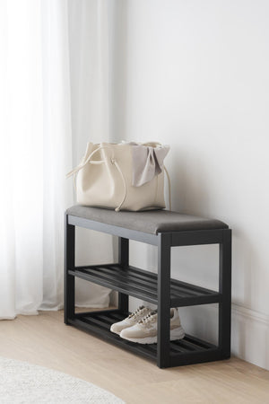Hallbänk med svart ram, grå dyna och skoförvaring, med beige väska och vita sneakers