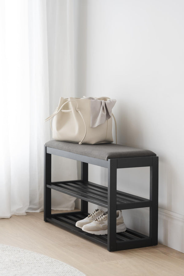 Hallbänk med svart ram, grå dyna och skoförvaring, med beige väska och vita sneakers