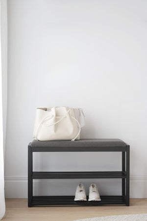 Skoförvaring med bänk i svart metall med grå dyna, vit väska och vita sneakers i minimalistisk hall