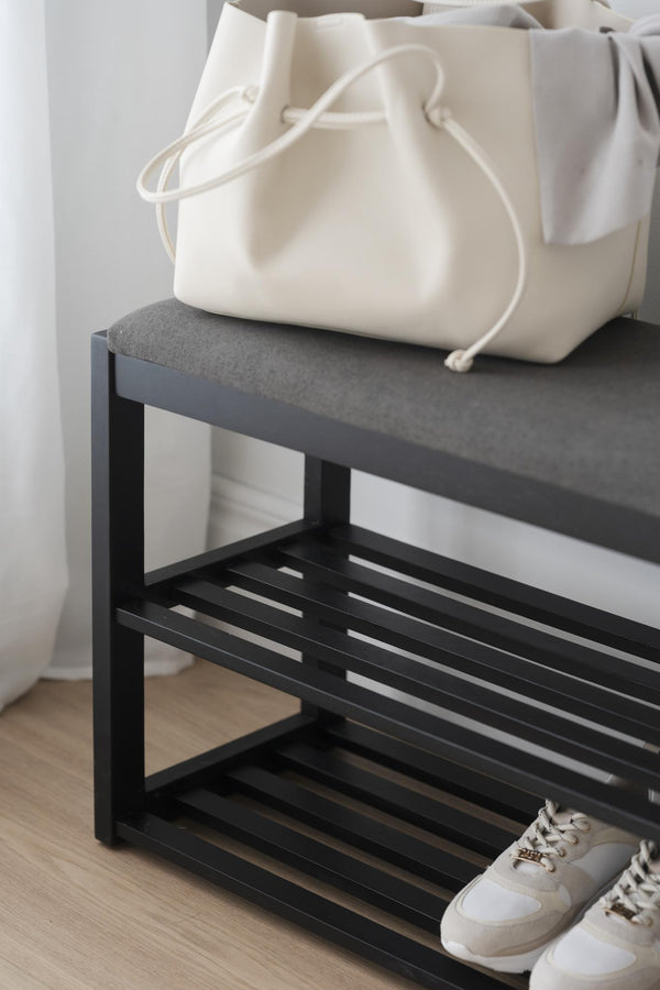 Skoställ i svart metall med tre hyllplan och grå topp, vit väska och vita sneakers