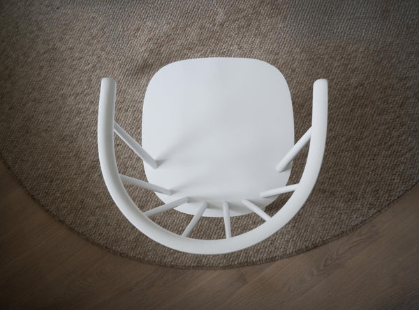 Vit stol uppochned på rund jutematta, ovanifrån fotograferad med synliga ben och sits