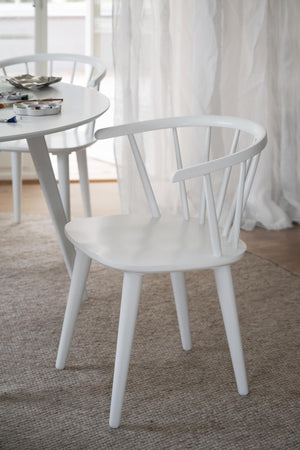 Vit pinnstol i skandinavisk design med rundad rygg och spjälor, placerad vid matbord på ljus matta