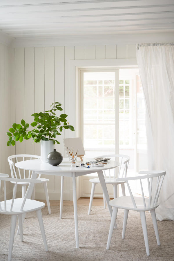 Vit rund matgrupp med spjälstolar i ljust skandinaviskt kök med växt och fönster