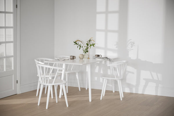 Vit matgrupp med runt bord och fyra pinnstolar i ljust skandinaviskt kök med trägolv