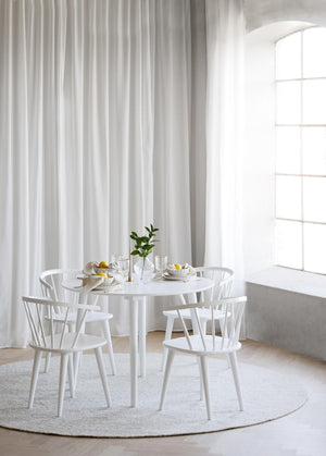 Vit matgrupp med runt bord och fyra pinnstolar i ljust matrum med långa gardiner