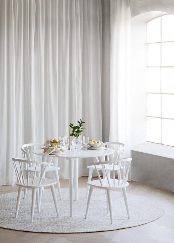 Vit matgrupp med runt bord och fyra pinnstolar i ljust matrum med långa gardiner