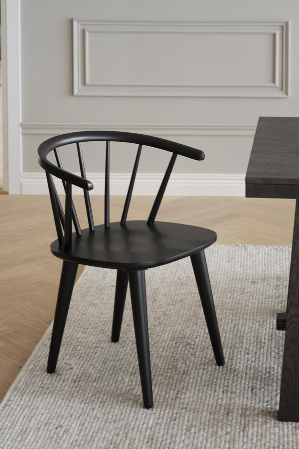 Svart träspindelsyol med rundad rygg och spjälor vid matbord på ljus matta