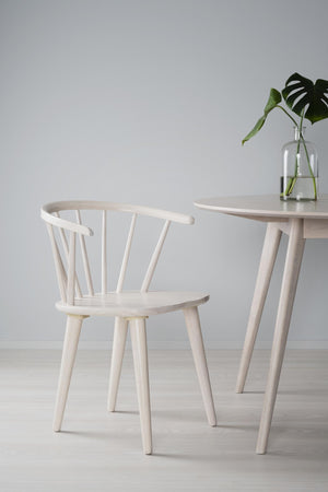 Ljus trässtol i skandinavisk design med spjälor i ryggen och matchande sidobord med monstera i glasvas