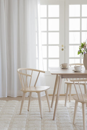 Ljus matgrupp i trä med runda stolar och rundt bord på vit matta vid glasdörr