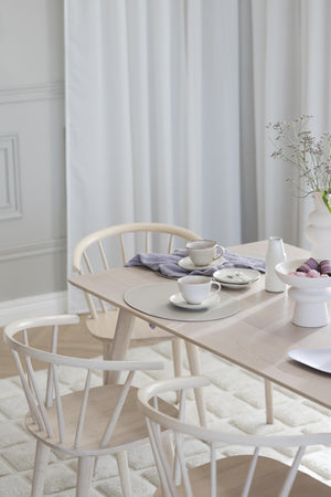Ljust matbord i trä med vita Windsor-stolar och porslin i skandinavisk stil