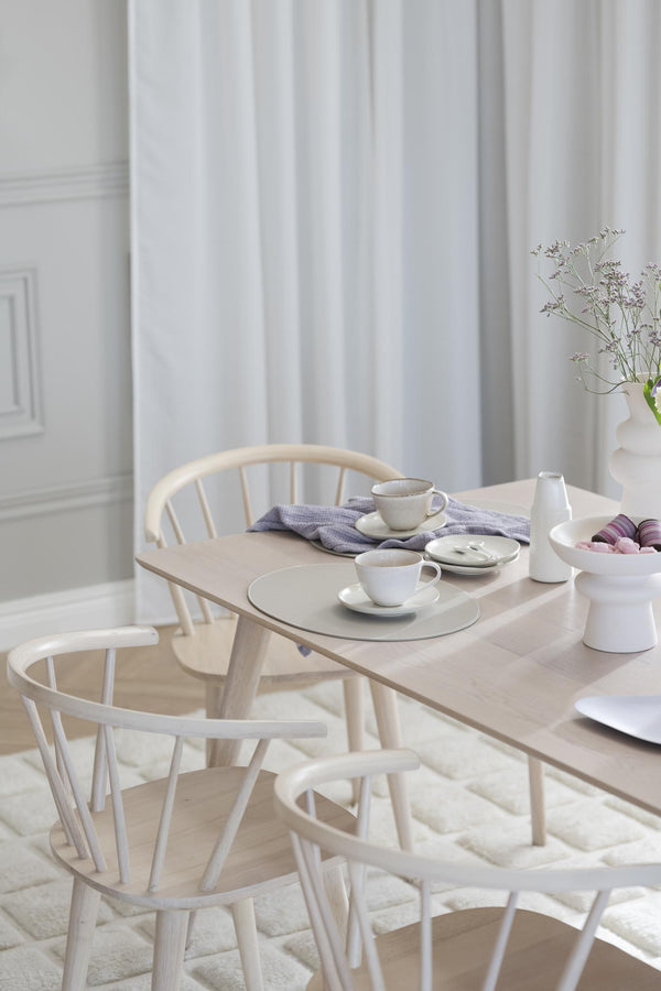Ljust matbord i trä med vita Windsor-stolar och porslin i skandinavisk stil