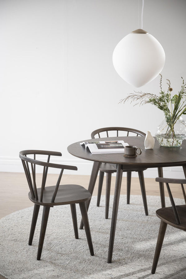 Runt matbord i mörkbejsat trä med matchande pinnstolar och vit taklampa i nordisk stil