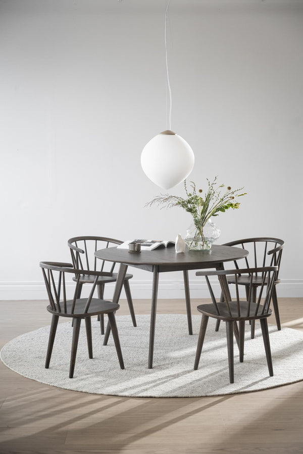 Matgrupp i mörkt trä med runt bord och fyra pinnstolar under vit taklampa på ljus rund matta
