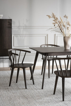 Mörkt matbord i trä med matchande stolar i skandinavisk design, dekorerat med torkade blommor i vas