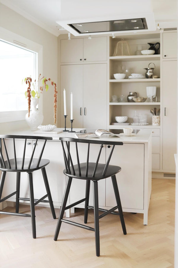 Vitt kök med öppen förvaring, svarta barstolar och minimalistisk inredning i skandinavisk stil