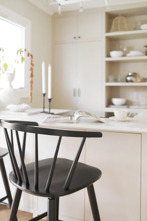 Svart trästol vid vitt köksbord i skandinavisk minimalistisk köksmiljö med öppna hyllor