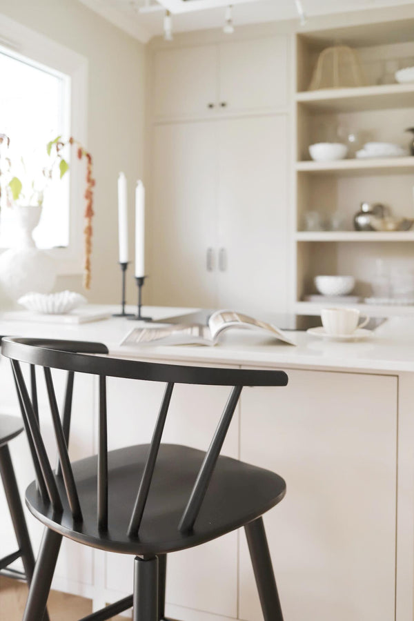 Svart trästol vid vitt köksbord i skandinavisk minimalistisk köksmiljö med öppna hyllor